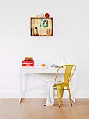 Books, pens and ornaments on and in wooden crate with patterned back panel mounted on wall; small desk and yellow, retro metal chair