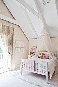 Vintage Kinderbett mit Baldachin an Dachschräge aufgehängt neben Fenster mit gerafftem Vorhang