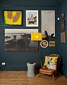 Kleiner Vintage Sessel neben Stehleuchte mit gelbem Lampenschirm vor blaugrau getönter Wand und Bildersammlung