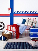 Vintage bed with red metal frame and candlesticks on blue metal box on castors in front of wave motif painted on wall