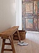 Trainers below rustic bench and rattan basket on wooden floor; weathered door in background