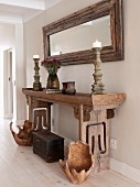 Gefässartige Objekte aus Holz und Truhe auf Boden vor rustikal antikem Wandtisch mit Kerzenleuchtern und gerahmter Spiegel an Wand