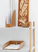 Holzobjekte in weisser Umgebung - Halbhohes Regal mit Fachböden aus weißem Metall und Büroutensilien aus Holz neben geschnitzter Holzplatte mit Tiermotiven