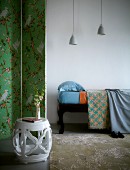 Weisser Beistelltisch mit rautenförmiger Schnitzerei vor Paravent im Vintagestil und Tagesbett unter schlichten Hängeleuchten