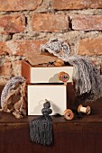 Stacked boxes painted white and haberdashery items on wooden chest of drawers against rustic brick wall