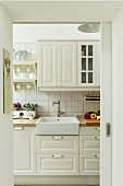 View through open sliding door into pale, country-house kitchen with vintage taps on Belfast sink