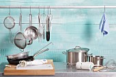 Assorted kitchen utensils on a stainless steel unit and hanging on a metal rod