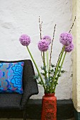 Zwiebelblüten in einer Vase neben Sessel mit Dekokissen