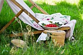 A deckchair with cushions, a straw hat and redcurrants next to a picnic basket