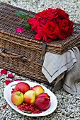 Rote Rosen auf Picknickkorb, daneben Obstteller