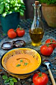 Eine Schüssel Gazpacho auf Gartentisch mit frischen Tomaten und Olivenöl