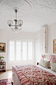 Double bed with floral blanket and pendant lamp with glass lampshades hanging from stucco ceiling