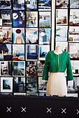 Tailors' dummy wearing green lady's jacket in front of colourful wall of photographs