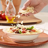 A spaghetti dish being sprinkled with parmesan