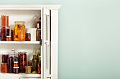 Preserved fruit in jars and bottles in an open kitchen cabinet