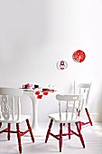 Old wooden chairs painted white and red around set, round, white table on white wooden floor against white wall