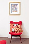 Scatter cushions on retro chair with red upholstery below framed picture on wall