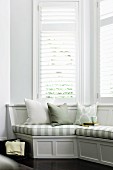 Comfortable, elegant, grey wooden window seat with striped seat cushions in white bay window with louver blinds - perfect for reading and relaxing