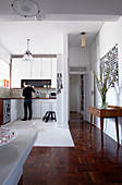 Open-plan interior with white fitted kitchen and hall area with mosaic parquet flooring and 50s console table