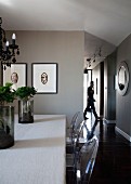 Artistic plant arrangements on dining table and Ghost chairs; framed artworks on taupe-painted wall and hallway to one side in background