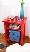 Books and blue cardboard boxes in bright red, open-fronted cabinet with various ornaments and accessories on top