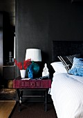 Bed & bedside table with table lamp against black wall