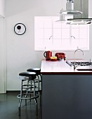 Retro bar stools at modern island counter with sink and gas hob below extractor hood
