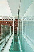 Loft gallery with glass floor and balustrade, steel joist structure against brick wall at far end and glass wall to one side