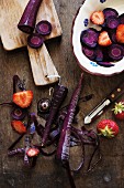 Violette Karotten und Erdbeeren, teilweise geschält und geschnitten, auf Holzbrett