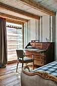 Partially visible bed with antique frame and chair at bureau in rustic bedroom