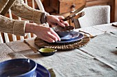 Woman setting table with cutlery, crockery & raffia placemat