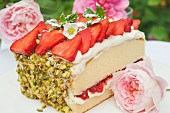 A slice of sponge cake with strawberries and pistachios on a garden table