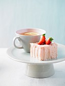 A cup of cake with strawberry buttercream, with a cup of tea