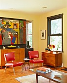 Gelbgetöntes Wohnzimmer mit roten Polsterstühlen im 50er Jahre Stil und bunte Malerei