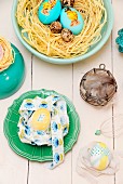 Various Easter nests of eggs, raffia and ribbons in bowls and on pale wooden surface