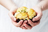 A woman's hands holding a brioche with caramel sauce and pistachios