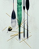 Scattered spaghetti next to a silhouette of a wine bottle, a glass and cutlery