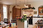 Open-plan, country-house kitchen with free-standing counter below suspended, overhead lighting unit; dining area with wrapped presents in foreground