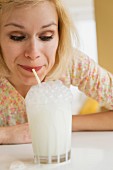A woman blowing through a straw into a glass of milk