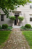 Paved path leading to stylish front door of white-painted, weatherboard country house