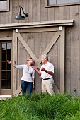 Man and woman talking and gesturing in front of large sliding door in wooden facade in rural surroundings