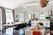Langer Esstisch mit Klassikerstühlen (Executive von Saarinen), Sitzbereich mit Sofa und offene Küche mit Frühstücksbar