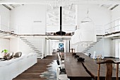 Rustikaler Massivholz-Tisch unter Hängeleuchten mit weißem Stoffschirm gegenüber Loungebereich in einer Loft-Wohnung