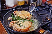 Pork chops frying in a pan with foamed butter and rosemary