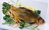 A fresh tench garnished with parsley, dill, carrots, leek and lemon slices