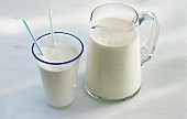 A jug of milk and a glass of milk with two drinking straws