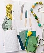 Fabric swatches in shades of green, yellow tulip, string of wooden beads and paint samples on wooden lolly sticks