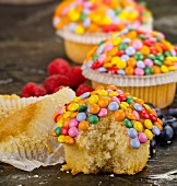 Cupcakes decorated with colourful chocolate beans, whole and with a bite missing