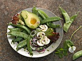 A plate of raw vegetables with sugar snap peas, avocado and mushrooms