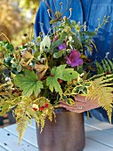 Woman's hands arranging autumnal bouquet in brown stoneware pot